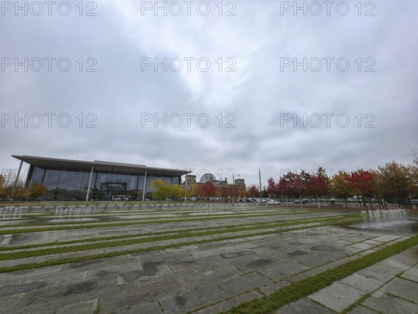 Extensive square with water fountains in the government district under heavy cloud cover in the background the Paul Löbe House, government district in 10557 Berlin, Germany
