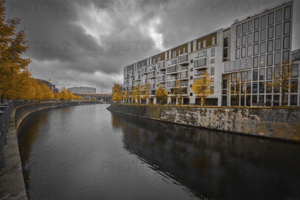 Modern apartment block on the river with yellow autumn trees, dramatic sky reflected in calm water, urban, melancholy atmosphere, at Berlin Central Station, 10557 Berlin, Germany