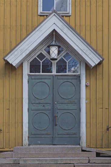 Closed old decorative double doors with white frame and window on top on a yellow board wall, Finland