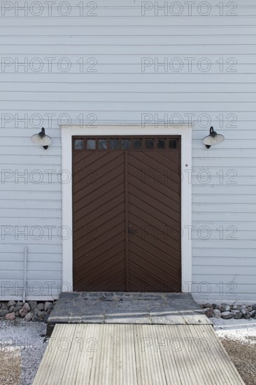 Closed old brown double doors with white frame and light blue board wall, Mustio, Finland
