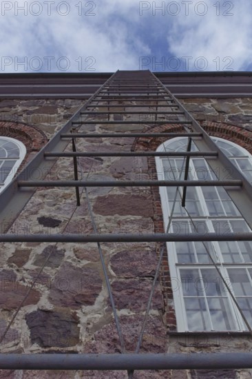 Metal ladder going up to the roof of a stone building, Karjalohja, Finland