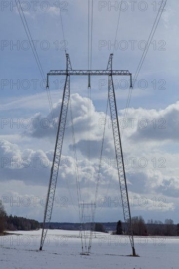 Steel tower with high voltage electric lines in cloudy winter weather with snow on the ground, Junkarsborg, Finland