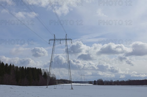 Steel tower with high voltage electric lines in cloudy winter weather with snow on the ground, Junkarsborg, Finland