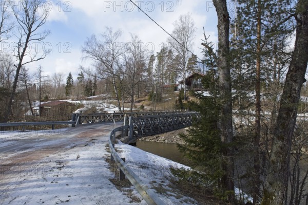 Gravel road on metal bridge over river Mustionjoki in winter, Junkarsborg, Finland