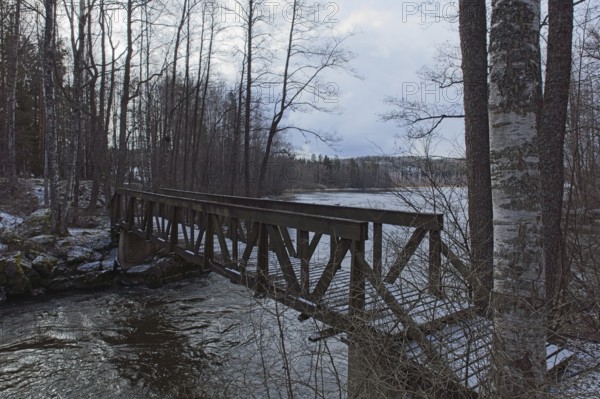 Old wood walking bridge over river Mustionjoki in cloudy winter weather, Junkarsborg, Finland