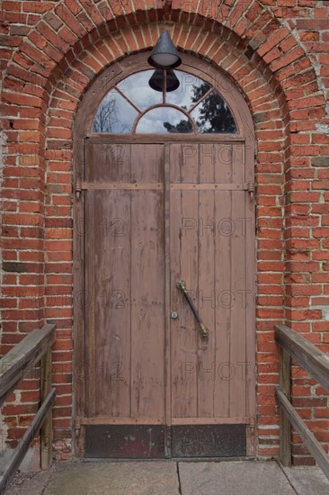Closed old brown double doors with arch window on top on a red brick wall, Karjalohja, Finland