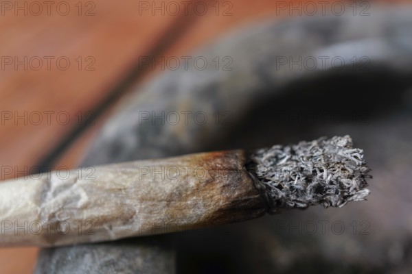 Close-up of a burning cigarette with a long ash resting on a dirty ashtray, symbolizing an unhealthy addiction