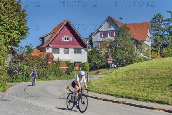 Country road with S-curve and two cyclists in Maria-Thann, Allgäu, Swabia, Bavaria, Germany