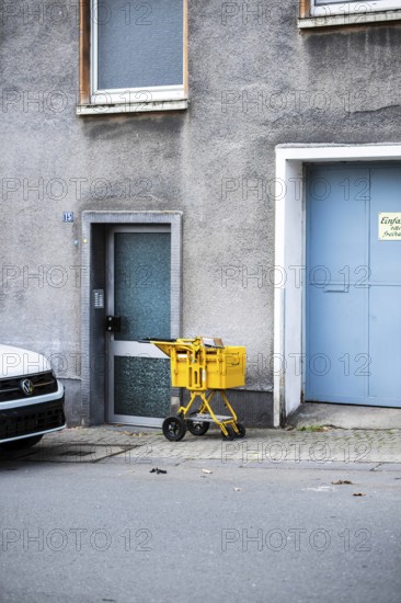 A yellow Deutsche Post delivery van stands in front of a grey façade between a front door and a large, light blue garage door, Wuppertal, Germany
