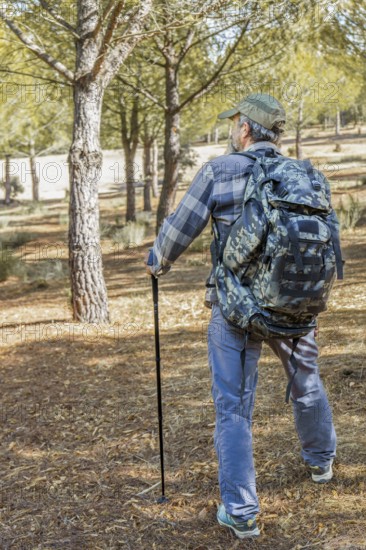Man walking an outdoor path, carrying a camouflage backpack and trekking pole, enjoying nature and adventure