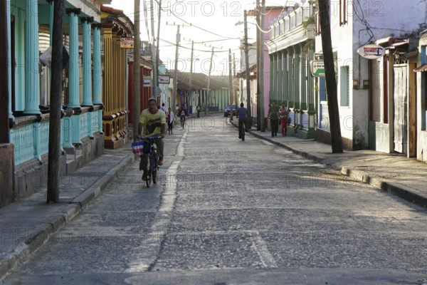 Baracoa, Cuba, Central America, narrow city street lively with cyclists and pedestrians in a colonial setting, Greater Antilles, Caribbean, America, Central America