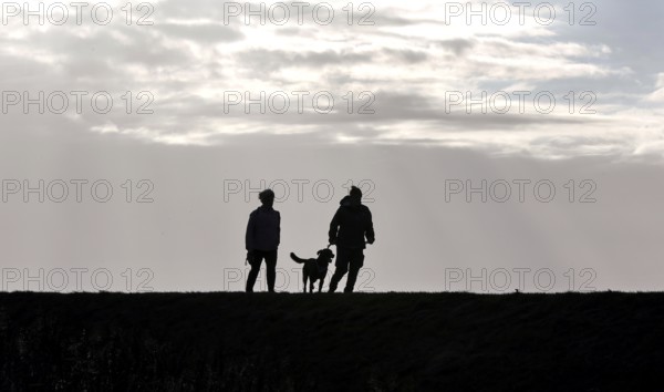 Couple with dog walking across a dike on the Baltic Sea, Fehmarn, 16.10.2025, Fehmarn, Schleswig-Holstein, Germany