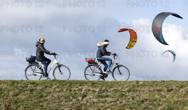 Cyclists ride across a dike and look at the sails of kite surfers, Fehmarn, 16.10.2025, Fehmarn, Schleswig-Holstein, Germany