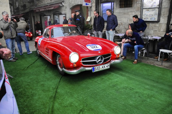 Roter 300 SL rolls across the green carpet through the old town, shiny chrome and rally number, lined with spectators, Mille Miglia 2016, time control, checkpoint, SAN MARINO, classic car racing. San Marino, Italia