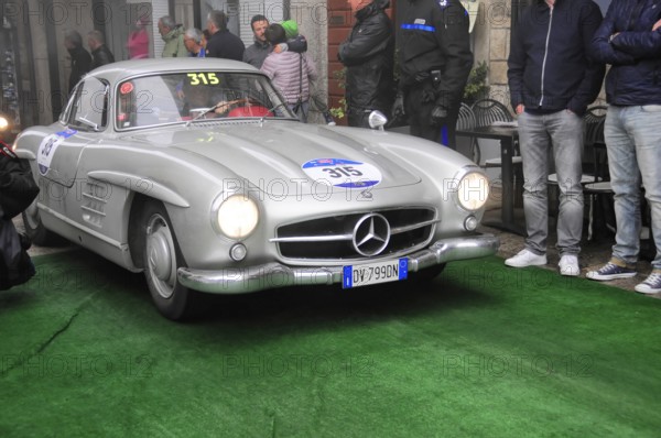 Silberner 300 SL drives through the old town with light over green carpet, surrounded by spectators in a humid, foggy rally atmosphere, Mille Miglia 2016, time control, checkpoint, SAN MARINO, classic car racing. San Marino, Italia