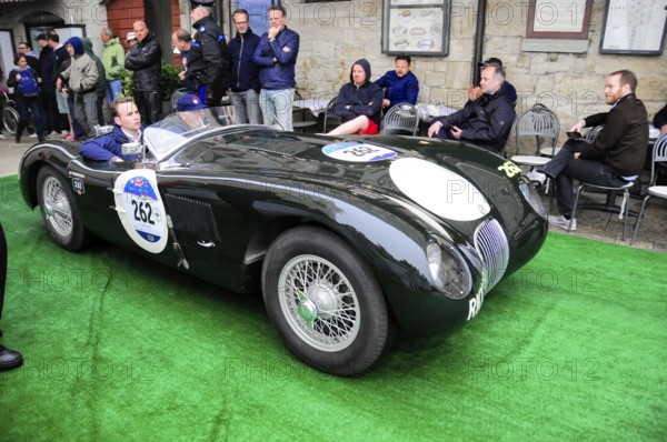 Black jaguar roadster rolls across green carpet during a historic rally, spectators sitting close to the sidelines, Mille Miglia 2016, time control, checkpoint, SAN MARINO, classic car racing. San Marino, Italia