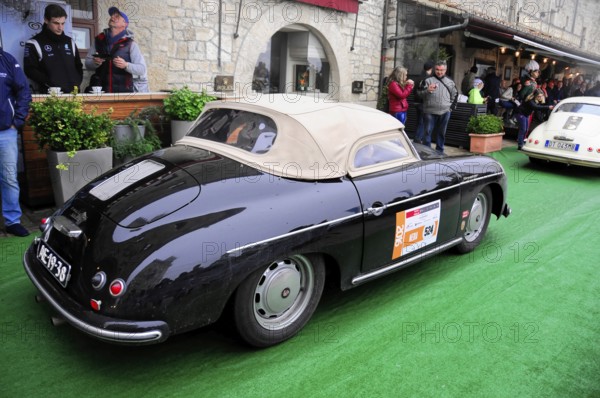 Black Porsche convertible with beige soft top drives relaxed through the old town at a classic car rally, Mille Miglia 2016, time control, checkpoint, SAN MARINO, classic car racing. San Marino, Italia