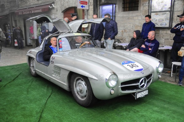 Silver 300 SL with open wing doors presents itself on the green carpet, interested audience in the old town, Mille Miglia 2016, time control, checkpoint, SAN MARINO, classic car racing. San Marino, Italia