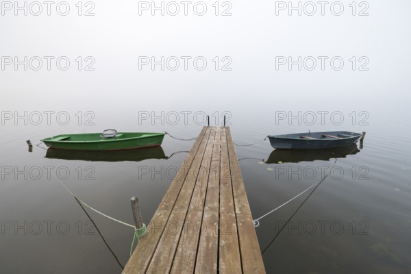 Two boats on a jetty on still, foggy water, Hopfensee, Ostallgäu, Bavaria, Germany