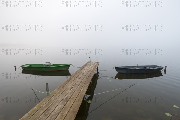 Two boats are moored on a wooden pier in fog, the atmosphere is calm and peaceful, Hopfensee, Ostallgäu, Bavaria, Germany