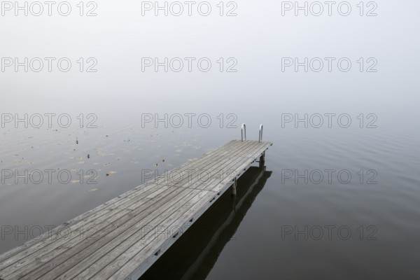 Empty wooden walkway in the misty water of a calm lake, Hopfensee, Ostallgäu, Bavaria, Germany