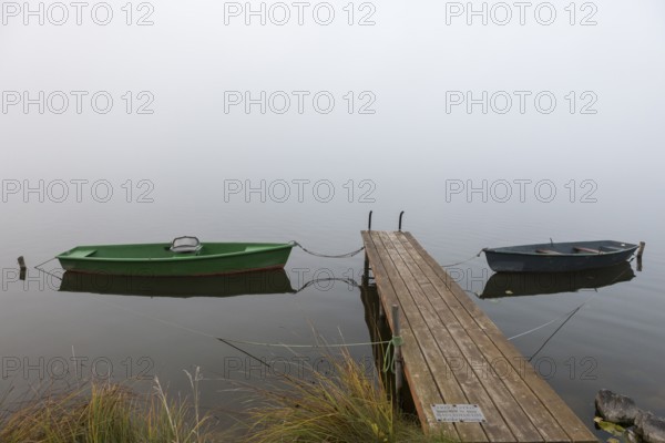 Two boats next to a wooden pier in a foggy, quiet autumn landscape, Hopfensee, Ostallgäu, Bavaria, Germany