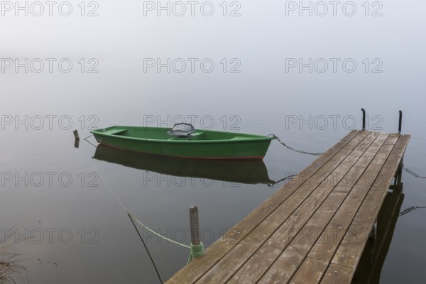 Single green boat on a wooden pier in fog, Hopfensee, Ostallgäu, Bavaria, Germany