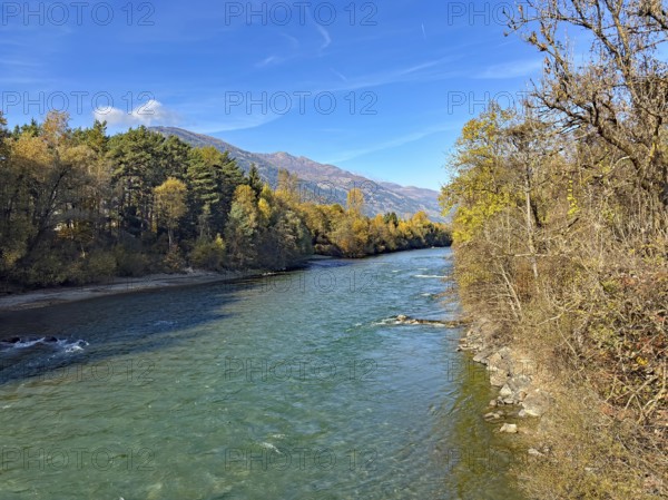 A quiet river surrounded by autumn trees and mountains under clear blue skies, Drau, Drauradweg, Lienz, Tyrol, Austria