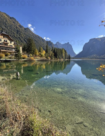 Clear water reflects the mountains and the house on the shore, Lake Toblach, Lake Dobbiaco, South Tyrol, Italy