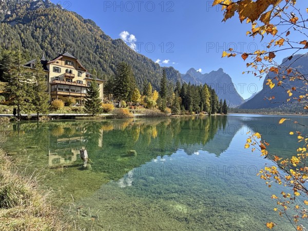 Clear water reflects the surrounding mountains and trees, a house on the shore, Lake Toblach, Lake Dobbiaco, South Tyrol, Italy