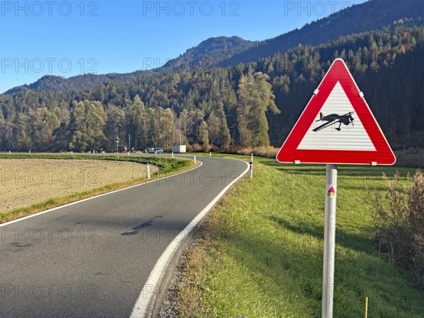 A country road with a warning sign for sailing leagues, under clear skies, surrounded by forests and mountains, Drau cycle path, Spittal, Carinthia, Austria