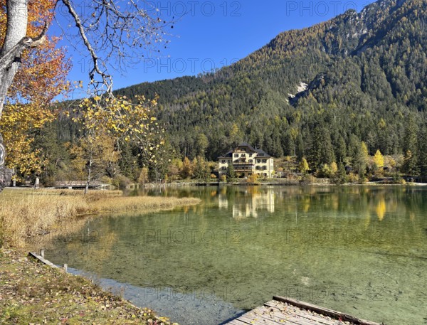 A lakeside villa surrounded by autumnal forests and clear reflection in the water, Lake Toblach, Lake Dobbiaco, South Tyrol, Italy