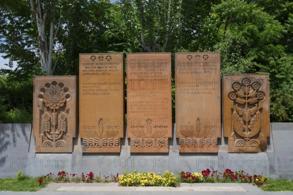 Stone monument with elaborate reliefs and surrounded by flowers, memorial plaques on Heroes' Alley in Victory Park, Haghtanak Park, Yerevan, Yerevan, Armenia