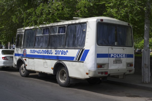 White police bus with Armenian lettering parked on the side of the road under shady trees, Yerevan, Yerevan, Armenia