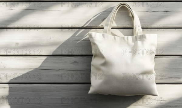A white canvas bag is hanging on a wooden surface. The bag is empty and has a shadow on the wall behind it. Scene is calm and peaceful, as the bag is hanging still and not being used. AI generated