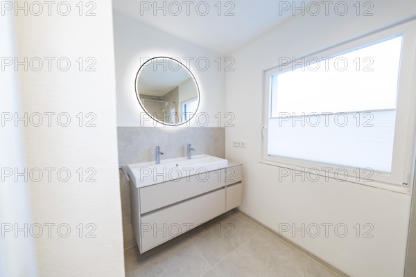 Bright bathroom with round illuminated mirror and double washbasin in front of subtle shades of gray, house renovation, energy renovation, Metzingen, Germany