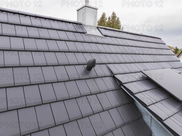 Detail of an anthracite-colored tile roof with roof vent and sheet metal connections under cloudy sky, house renovation, energy renovation, Metzingen, Germany