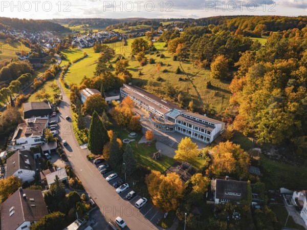 A school building between colorful autumn trees and hills in a village, Deufringen, Aidlingen, Böblingen district, Germany