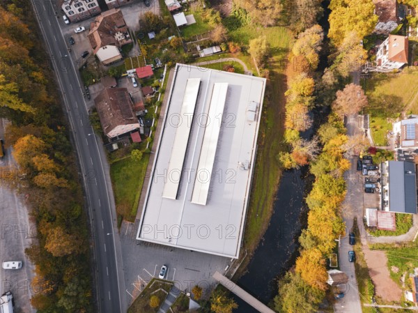 Aerial view of a sports hall in autumn-colored surroundings with adjacent river, Walter Lindner Sporthalle Calw, Black Forest, Germany