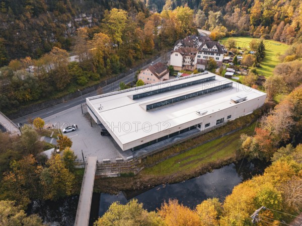 Sports hall nestled in an autumnal setting with a small river and bridge nearby, Walter Lindner Sporthalle Calw, Black Forest, Germany
