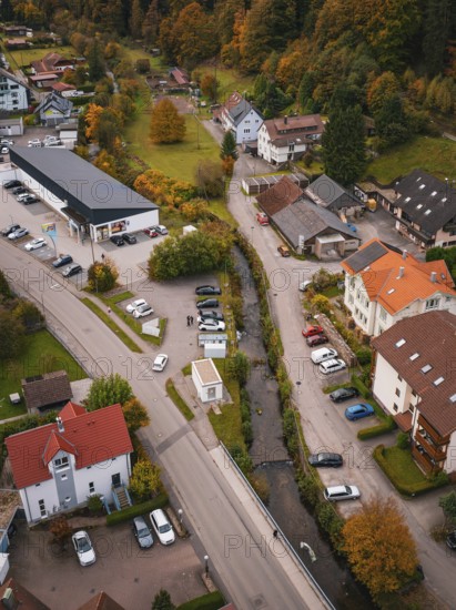Aerial view of a small village in autumn with colorful trees, roads, buildings and a small river, Calmbach, Bad Wildbad, Black Forest, Germany