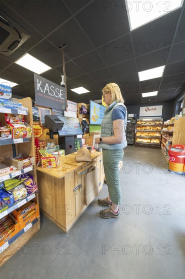 A woman stands at the cash register in a supermarket with snacks and products on the shelves, 24 hours Aunt M Store
