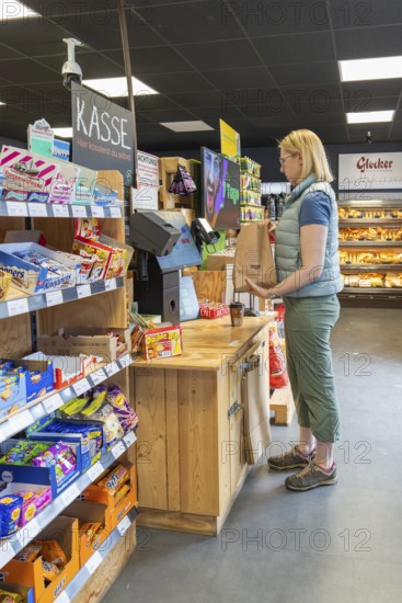 A woman sticks a brown shopping bag near the cash register, surrounded by products, 24 hours Aunt M Store