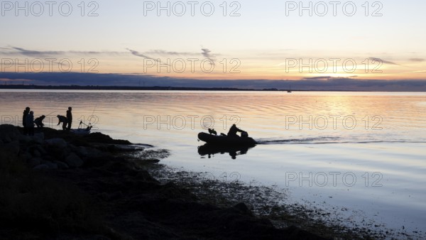 Angler on the beach during sunset, an angler docks on the shore with his inflatable boat and dog, Fehmarn island, 18.10.2025, Fehmarn, Schleswig-Holstein, Germany