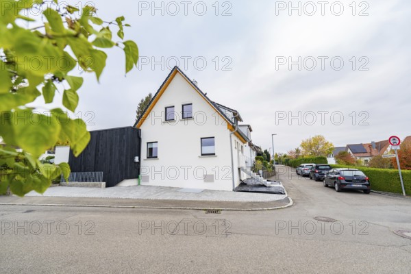 Side view of a bright residential building in a quiet settlement with parked cars and hedges, house renovation, climate renovation, Metzingen, Germany