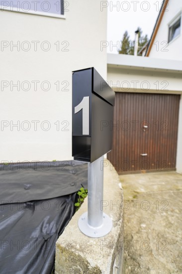 Close-up of a modern black mailbox in front of garage and plaster façade, house renovation, climate renovation, Metzingen, Germany