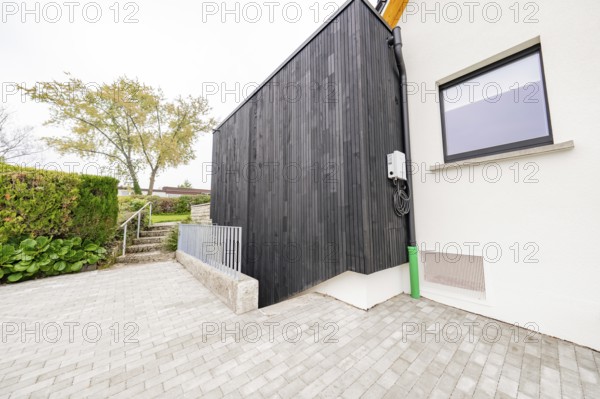 Modern house side with black wood paneling on paved driveway, house renovation, air conditioning renovation, Metzingen, Germany