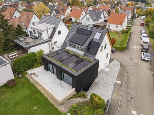 Angled aerial view of a modernized house with photovoltaic on gable roof and green extension in a well-maintained residential area, house renovation, climate renovation, Metzingen, Germany
