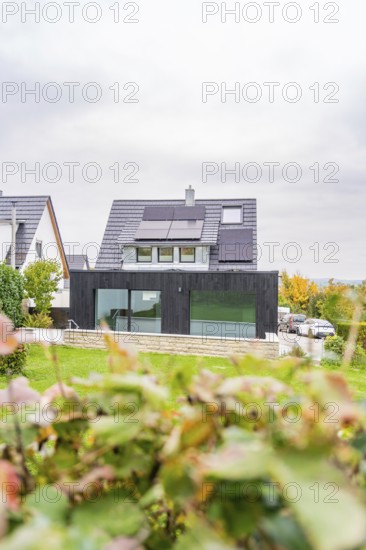 Residential building with black extension and glass front between neighboring houses, autumnal hedge in the foreground, quiet suburban atmosphere, house renovation, climate renovation, Metzingen, Germany