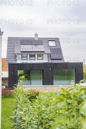 Front view of a house with solar panels and black extension with glass front, well-kept garden and quiet atmosphere, house renovation, air-conditioning renovation, Metzingen, Germany